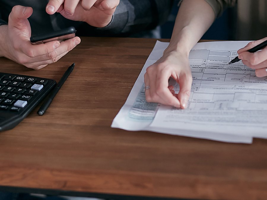 Dos personas revisando papeles y una calculadora sobre una mesa de madera