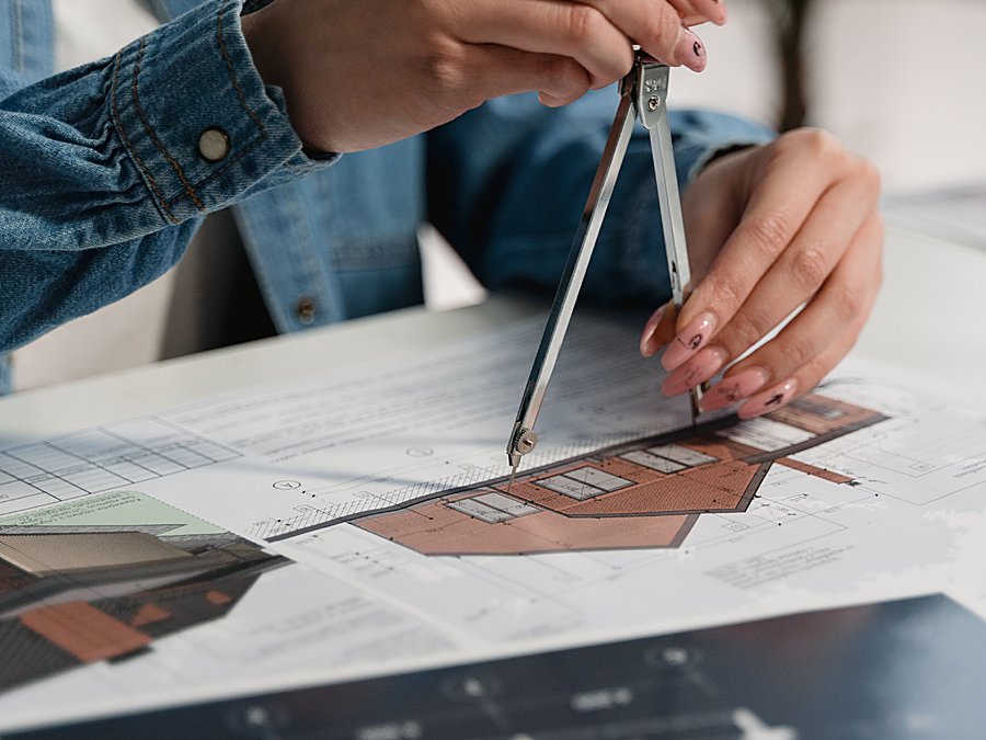 Manos dibujando un plano de vivienda con un compás sobre papel milimetrado